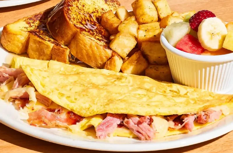 Omelette avec omelette garnie de jambon effiloché, bacon et fromage suisse. Servie avec rôtie, un choix parmi crêpe (1), crêpes fines (3) ou
