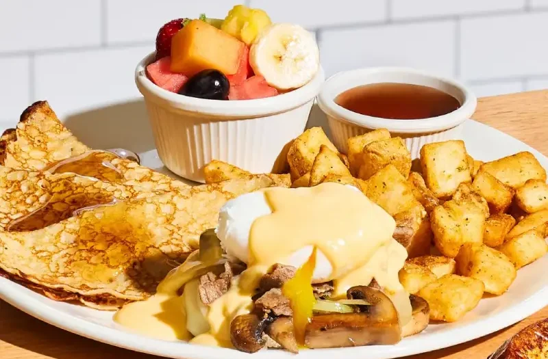 Béné philly avec un œuf poché servi sur muffin anglais avec steak Philly, oignons et champignons sautés, fromage Cantonnier et sauce fromagée