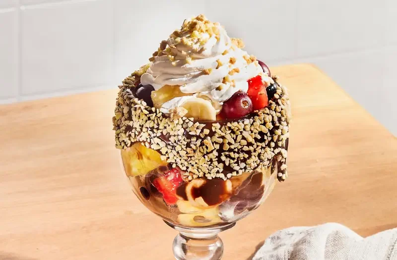 Coupe de fruits décadente avec fruits frais nappés de coulis au choix et garnis de crème fouettée, crumble de biscuits feuille d’érable dans une