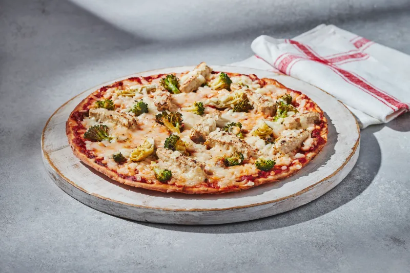 Veggie Protein pizza with plant-based chicken, pesto, artichoke hearts, broccoli, and plant-based mozzarella on a cauliflower crust