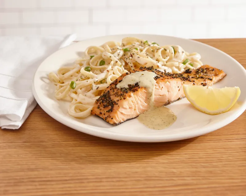 Saumon pesto avec filet de saumon nappé d’une sauce crémeuse Alfredo au pesto, le tout servi avec un quartier de citron et un accompagnement au