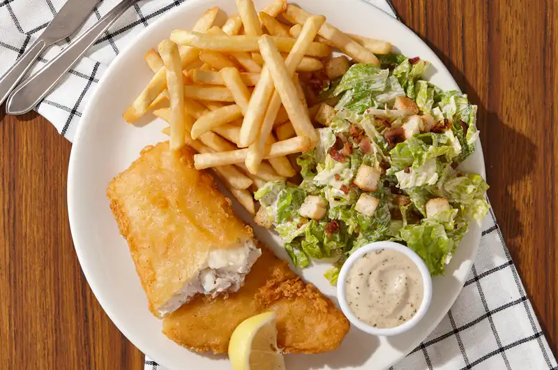 Fish & Chips avec généreux filet de poisson d’aiglefin pané servi avec une mayonnaise aïoli au basilic, une petite salade César et un
