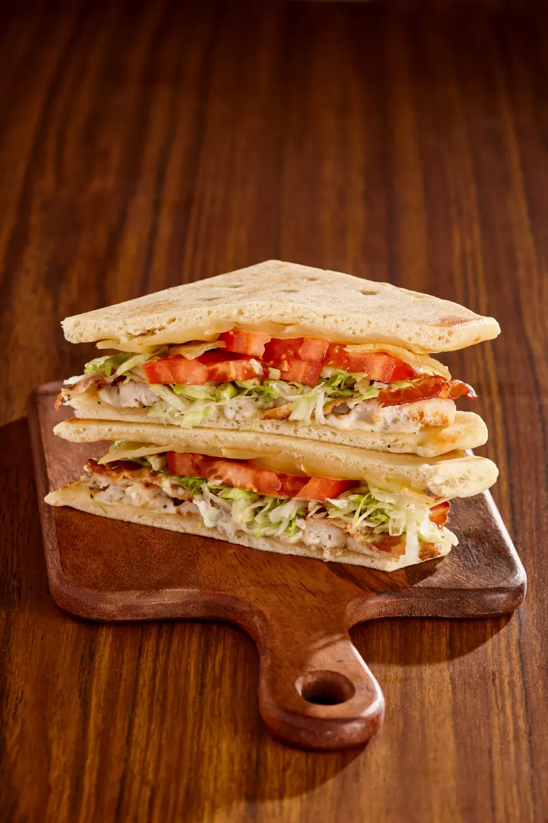 Focaccia Cantonnier Club with chicken breast strips, bacon, Cantonnier cheese, tomatoes, lettuce and basil aioli, served on a focaccia bun