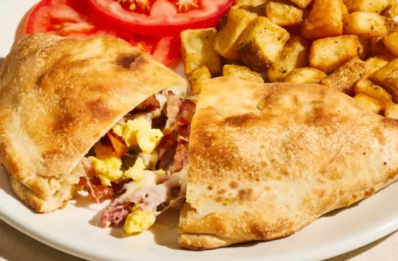 Panzerotti déjeuner avec chausson doré farci d’un œuf brouillé, jambon effiloché, bacon, champignons rôtis, fromage suisse et sauce hollandaise