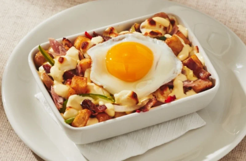 Poutine déjeuner avec oeuf(s) à ton goût servi(s) sur une délicieuse préparation gratinée composée de pommes de terre assaisonnées, jambon