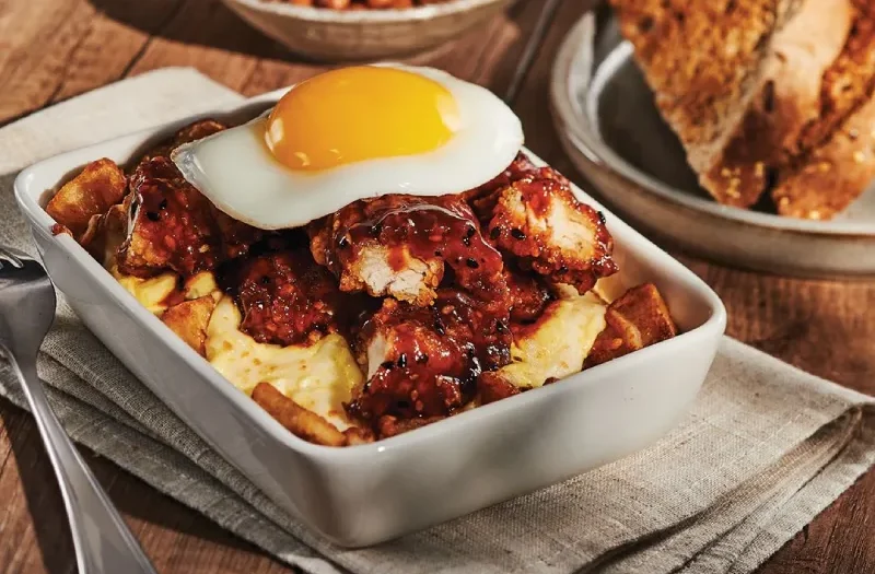 Poulet frit tao avec œuf(s) à ton goût servi(s) sur une délicieuse préparation gratinée composée de pommes de terre assaisonnées, poulet frit