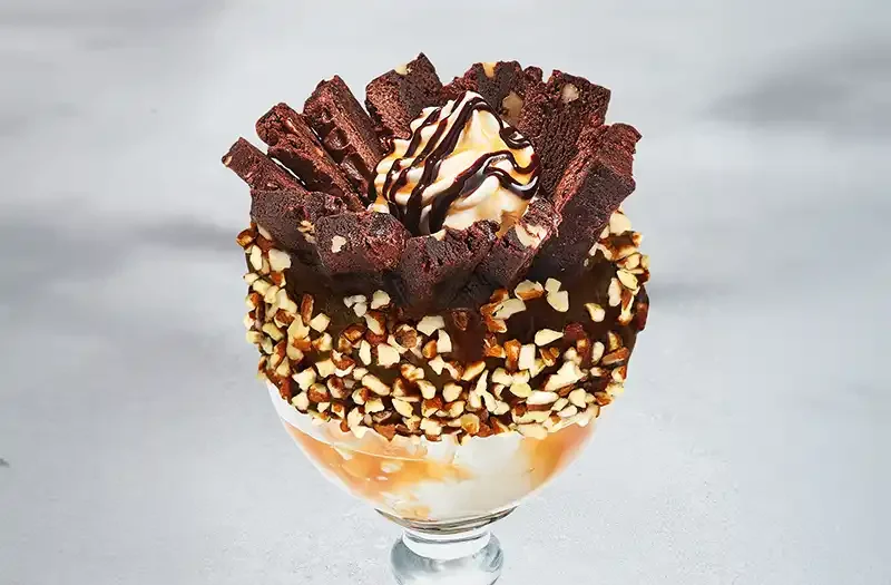 Volcano with a mountain of ice cream, brownies, whipped cream and caramel, all covered with a chocolate coulis and a rim dipped in chocolate