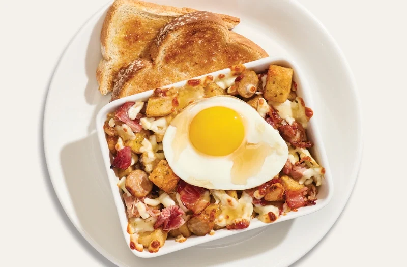 Chez nous avec œuf(s) à ton goût servi(s) sur une délicieuse préparation gratinée composée de pommes de terre assaisonnées, jambon effiloché