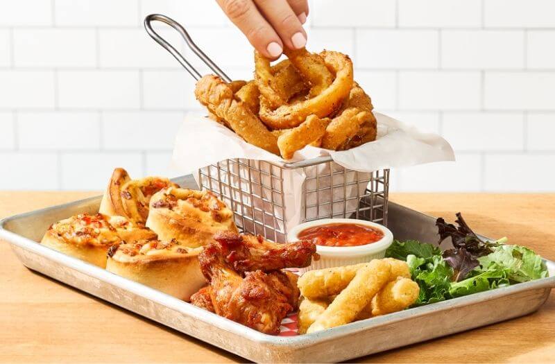 Mix Mikes avec 4 bâtonnets de fromage, 4 rouleaux pizza bruschetta, 4 ailes de poulet, rondelles d’oignon et 2 trempettes